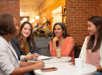 Four young ladies indulged in a conversation during coffee break in a workplace canteen